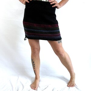 May include: A black mini skirt with a colorful geometric pattern around the hem. The skirt is made of a soft, knitted fabric.