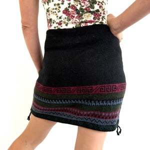 May include: Black knitted skirt with a colorful geometric pattern at the hem. The skirt has a drawstring at the side.