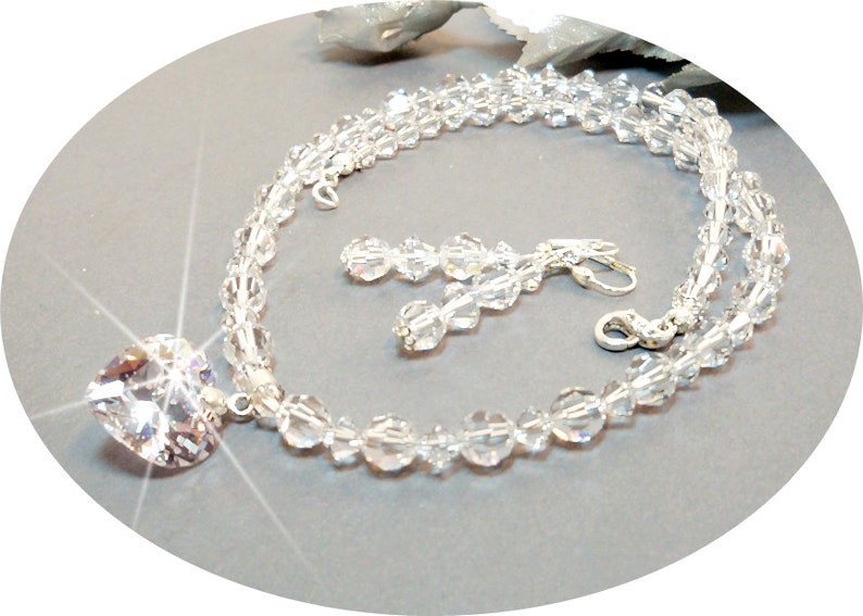 Puede incluir: Un conjunto de collar y pendientes de cristal con un gran colgante en forma de coraz&oacute;n. El collar est&aacute; hecho de cuentas de cristal transparente y los pendientes son de estilo colgante.