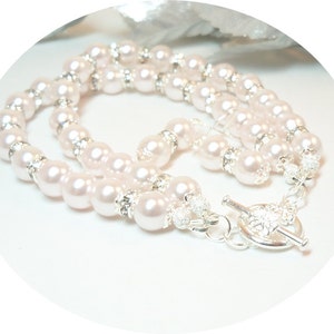 May include: A double strand pearl necklace with a silver toggle clasp. The pearls are white and have a slight iridescent sheen. The necklace is made of faux pearls and silver-toned metal.