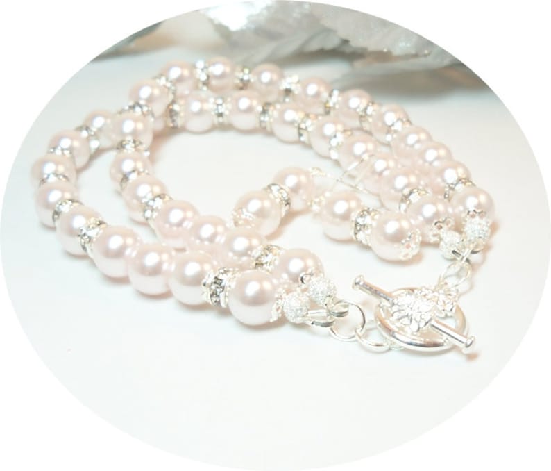 May include: A double strand pearl necklace with a silver toggle clasp. The pearls are white and have a slight iridescent sheen. The necklace is made of faux pearls and silver-toned metal.
