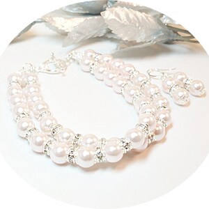 May include: A two-strand pearl bracelet and matching earrings set. The bracelet features white pearls and clear rhinestones. The earrings are silver with white pearls and rhinestones.
