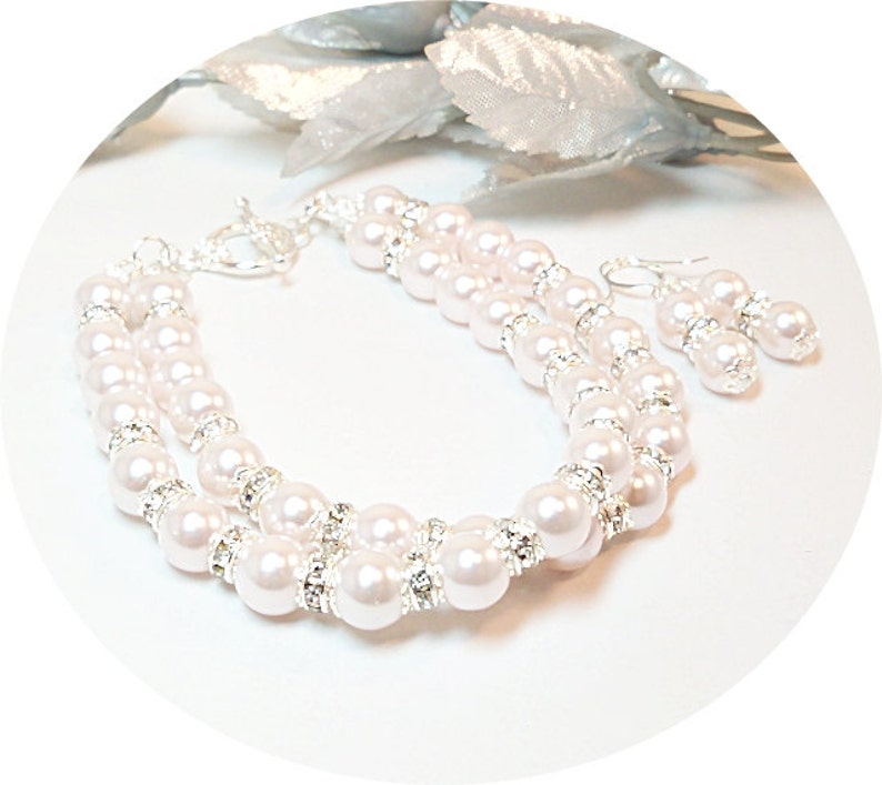 May include: A two-strand pearl bracelet and matching earrings set. The bracelet features white pearls and clear rhinestones. The earrings are silver with white pearls and rhinestones.