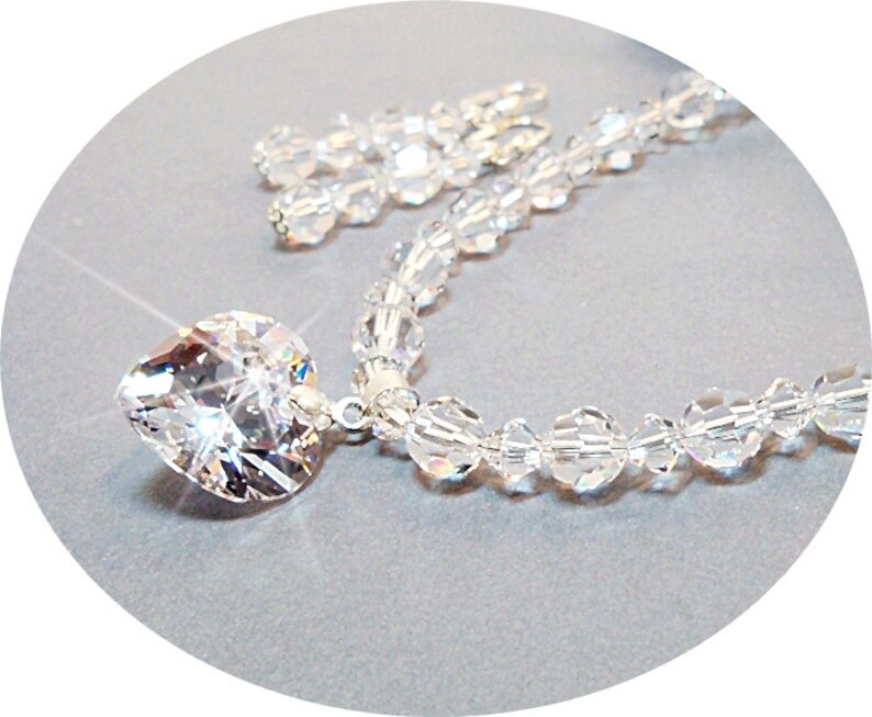 Puede incluir: Un collar de plata con un gran colgante de coraz&oacute;n de cristal y una cadena de cuentas de cristal.