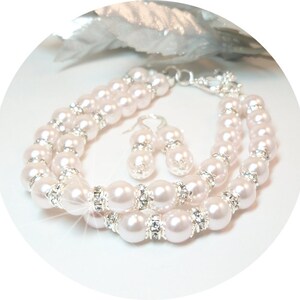 May include: A set of pearl jewellery featuring a double-strand bracelet and a pair of earrings. The pearls are a soft pink colour and are accented with clear rhinestones.