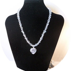 Puede incluir: Un collar de cristal con un gran colgante en forma de coraz&oacute;n. El collar est&aacute; hecho de cuentas de cristal transparentes y el colgante tambi&eacute;n es transparente.