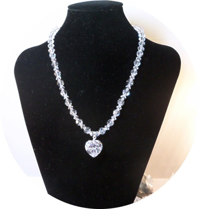 Puede incluir: Un collar de cristal con un gran colgante en forma de coraz&oacute;n. El collar est&aacute; hecho de cuentas de cristal transparentes y el colgante tambi&eacute;n es transparente.