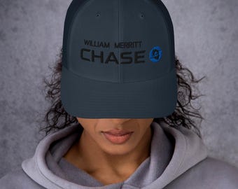 Op de afbeelding: Een donkerblauwe truckercap met een zwart mesh-achterpaneel. De cap heeft de tekst "William Merritt Chase" in het zwart geborduurd op de voorkant.