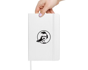 May include: A white notebook with a black and white illustration of a man's portrait in a circle. The notebook has a matching white elastic band and a ribbon bookmark. The notebook is held by a hand with painted nails.