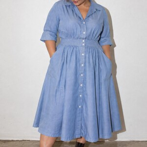 May include: A light blue midi-length shirt dress featuring a collared neckline, three-quarter length sleeves, and a button-down front closure. The dress has a fitted waistline with a full, pleated skirt and side pockets, paired with black lace-up boots.