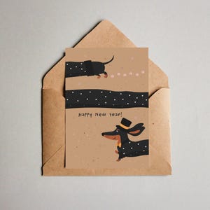 May include: A greeting card featuring a dachshund illustration with a top hat and bow tie, set against a tan background. The card reads "Happy New Year!" and is placed inside a brown envelope. The dachshund is black with white polka dots.