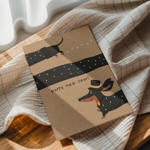 May include: A greeting card with a dachshund illustration. The card features a brown background with black polka dots and the text "Happy New Year!". The dachshund is wearing a top hat and bow tie. The card is resting on a beige cloth.