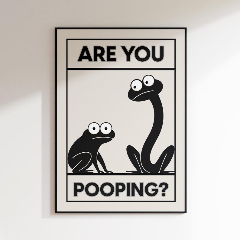 May include: Black and white framed art print featuring two cartoon frogs with large eyes. The text "ARE YOU POOPING?" is displayed in bold, uppercase letters, adding a humorous touch to the artwork. The print has a neutral background.
