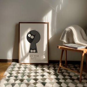 May include: Framed art print featuring a cartoon cat peering through a keyhole. The cat is black and gray with large white eyes. The text "I SEE YOUR BUTT" is below the cat. The frame is brown.