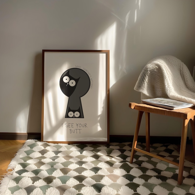 May include: Framed art print featuring a cartoon cat peering through a keyhole. The cat is black and gray with large white eyes. The text "I SEE YOUR BUTT" is below the cat. The frame is brown.