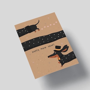 May include: Greeting card with a tan background featuring two dachshunds. One dachshund is wearing a top hat and bow tie. The card has the text "Happy New Year!" and a black dotted stripe.