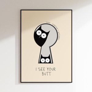 May include: A framed art print featuring a whimsical cat design. The artwork depicts a black cat peeking through a keyhole, with the text "SHHH... SOMEONE'S WATCHING!" and "I SEE YOUR BUTT" below. The background is a light beige.