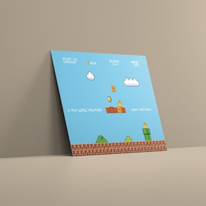Puede incluir: Una impresi&oacute;n en lienzo azul con una escena de videojuego pixelada con texto que dice "PLAY 01", "A NEW LEVEL UNLOCKED" y "HAPPY BIRTHDAY". La obra de arte incluye nubes, monedas y una plataforma de ladrillos.