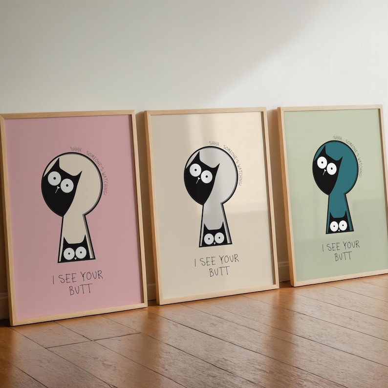 May include: Three framed art prints with a humorous cat design. Each print features a black cat silhouette within a keyhole shape, with the text "I SEE YOUR BUTT" below. The backgrounds are pastel pink, cream, and mint green.