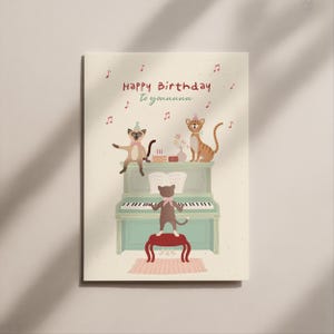 Könnte beinhalten: Geburtstagskarte mit einer skurrilen Illustration von Katzen. Die Karte zeigt ein hellgrünes Klavier, einen roten Hocker und Noten. Der Text "Happy Birthday to youuuuu" ist in Rot geschrieben.