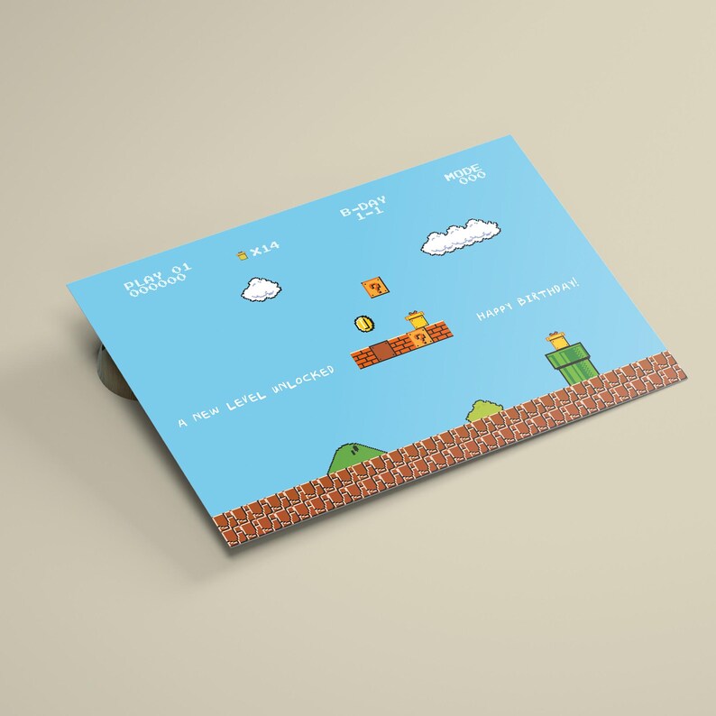 Puede incluir: Una tarjeta azul con un dise&ntilde;o de videojuego retro, que incluye gr&aacute;ficos pixelados de nubes, monedas y plataformas. La tarjeta tiene el texto "Happy Birthday!" y "A New Level Unlocked".