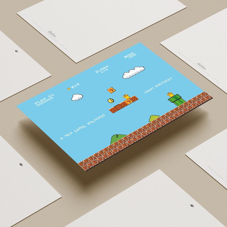 Puede incluir: Una postal azul con un dise&ntilde;o de videojuego pixelado, con el texto "Happy Birthday!" y "A New Level Unlocked." La imagen presenta nubes, monedas y una plataforma de ladrillos. Otras postales blancas rodean la tarjeta principal.