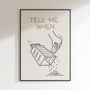 Puede incluir: Un dibujo en blanco y negro de una mano rallando queso en un rallador. El texto "TELL ME WHEN" está escrito en dorado sobre la imagen.