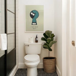 May include: A bathroom scene featuring a white toilet, a framed art print with the text "I SEE YOUR BUTT", and a potted plant. The floor has a black and white tile pattern. A roll of toilet paper and a soap dispenser are on the toilet tank.