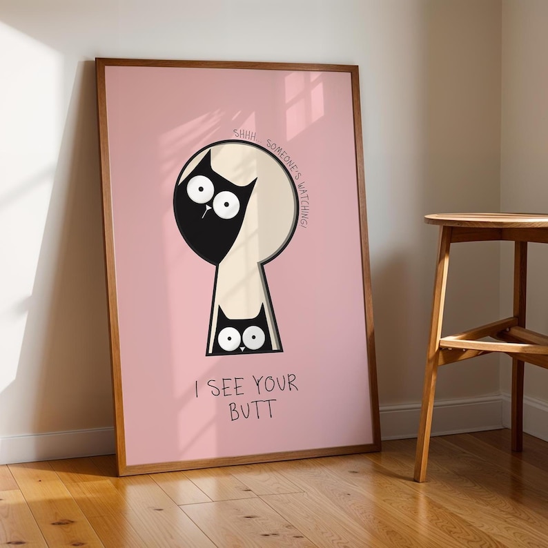 May include: Framed art print featuring a black cat peering through a keyhole shape on a pink background. The text reads "SHHH SOMEONE'S WATCHING" and "I SEE YOUR BUTT". The artwork is in a wooden frame.