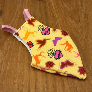 May include: A yellow fabric bird toy with pink straps. The fabric has a repeating pattern of butterflies, hearts, deer, and roses.