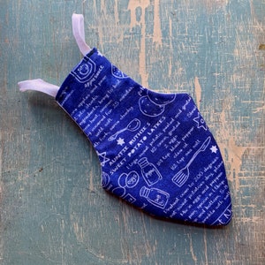May include: A blue fabric stocking with a white elastic loop. The stocking features a recipe for sweet potato latkes, with white illustrations of ingredients and cooking utensils. The text includes the recipe title, ingredients, and instructions.