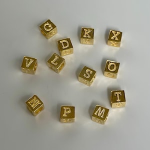 May include: A set of gold-colored letter beads, each with a different letter of the alphabet. The letters include G, K, X, D, L, V, S, O, M, P, and T.