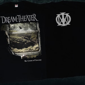 Könnte beinhalten: Schwarzes T-Shirt mit einem weißen Aufdruck der Band Dream Theater und dem Albumtitel "The Count of Tuscany". Auf der Rückseite des Shirts befindet sich ein weißes Logo mit den Initialen der Band.