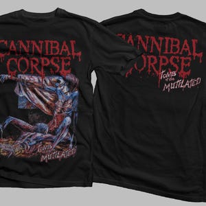 Puede incluir: Camiseta negra con el nombre de la banda "Cannibal Corpse" en fuente roja goteante en la parte delantera y trasera. El gráfico frontal representa una ilustración espantosa. La parte trasera de la camiseta también muestra "Tombs of the Mutilated".