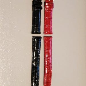 May include: Two watch straps, one black and one red, with gold buckles. The straps are made of leather and have a crocodile pattern.