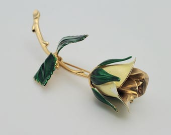 May include: A gold-tone brooch in the shape of a white rose with green leaves and a stem.