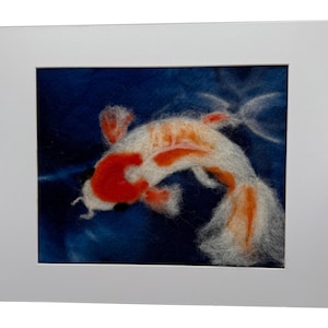 May include: A framed artwork featuring a koi fish. The fish is white with orange and red markings, set against a deep blue background. The artwork is presented in a white mat and frame, creating a clean, modern aesthetic.