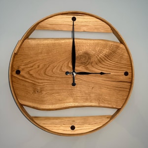 May include: A round wooden wall clock with black hands and a natural wood finish. The clock face is surrounded by a wooden frame with a decorative cutout.