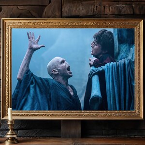 May include: A framed print featuring a scene from a movie. The image shows a bald character in a dark blue robe with his mouth open and arm raised. Another character is in the background, wearing a red shirt. The frame is gold.
