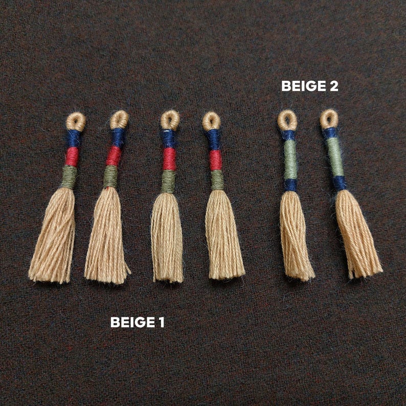 Pode incluir: Sete borlas bege com detalhes azuis, vermelhos e verdes. As borlas est&atilde;o dispostas em fila, com o texto "BEIGE 1" abaixo das quatro primeiras borlas e "BEIGE 2" acima das tr&ecirc;s &uacute;ltimas borlas.