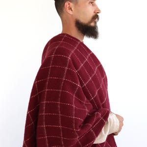 Pu&ograve; includere: Un uomo indossa uno scialle rosso e bianco a quadri con frange. Lo scialle &egrave; fatto di un tessuto morbido e caldo, perfetto per tenersi al caldo in inverno.