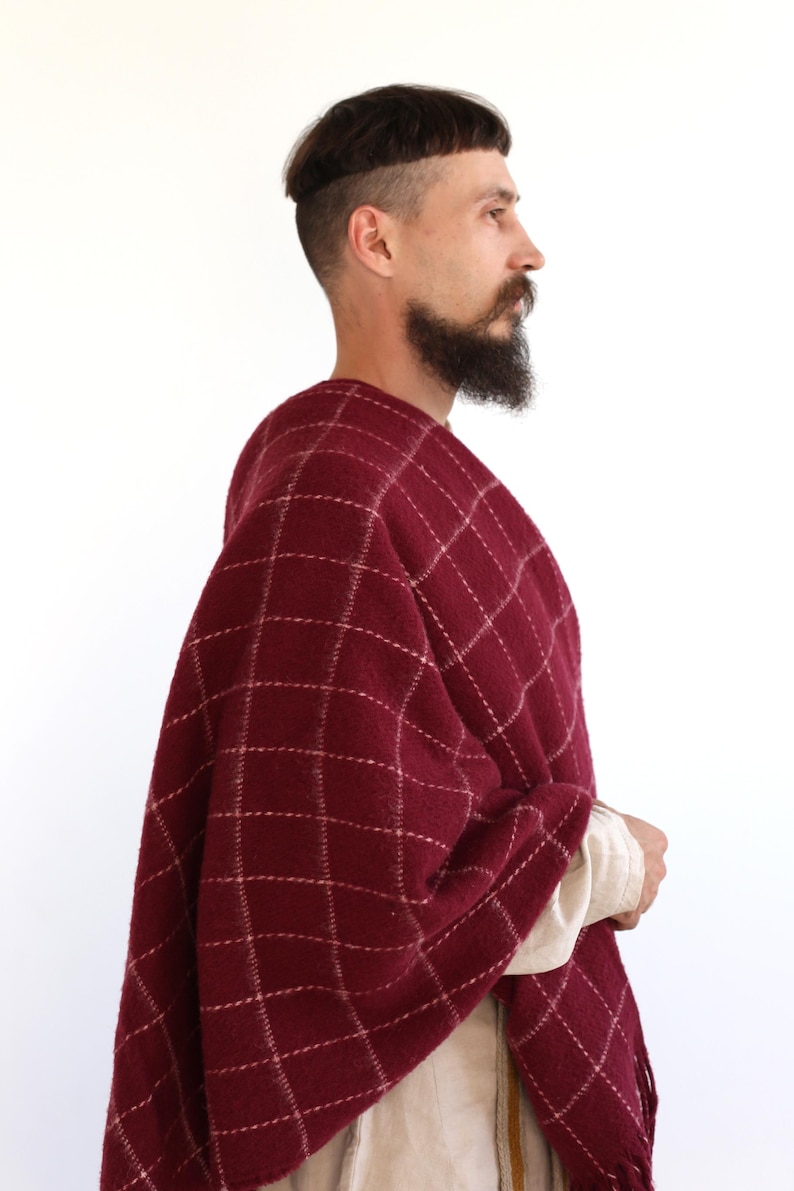 Pu&ograve; includere: Un uomo indossa uno scialle rosso e bianco a quadri con frange. Lo scialle &egrave; fatto di un tessuto morbido e caldo, perfetto per tenersi al caldo in inverno.
