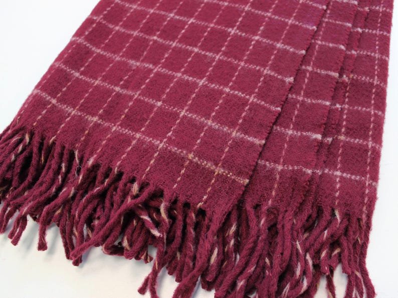 Pu&ograve; includere: Una sciarpa a quadri bordeaux con frange bianche. La sciarpa &egrave; realizzata in un materiale morbido e soffice.