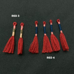 Pode incluir: Seis borlas vermelhas com detalhes azuis e brancos. As borlas est&atilde;o dispostas em fila, com o texto "RED 3" acima das tr&ecirc;s primeiras borlas e "RED 4" abaixo das tr&ecirc;s &uacute;ltimas borlas.