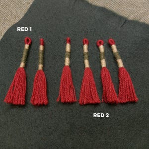 Pode incluir: Sete borlas vermelhas com detalhes verdes e bege. As borlas est&atilde;o dispostas em duas filas, etiquetadas como "RED 1" e "RED 2".