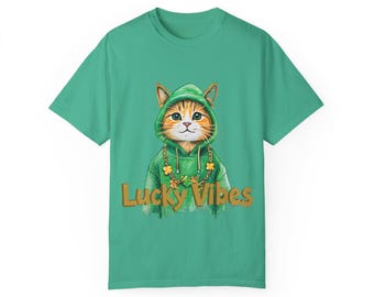 May include: A green t-shirt with a cartoon cat wearing a green hoodie and a gold shamrock necklace. The cat has orange and white fur. The words "Lucky Vibes" are printed in gold across the bottom of the graphic.