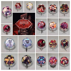 May include: A selection of illuminated badge reels with cartoon character designs. Each reel has a clear plastic base, a beaded border, and a retractable cord. The designs feature characters from the animated series "Hazbin Hotel". The image also shows the "Hazbin Hotel" sign.