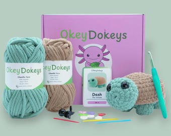 May include: A craft kit with chenille yarn, crochet hook, and a crochet turtle. The kit includes a pink box with the text "Okey Dokey's" and a cartoon axolotl. The yarn is teal and tan. The finished turtle is teal and tan.