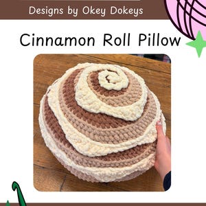 May include: A handmade cinnamon roll pillow in shades of cream, tan, and brown. The pillow is round with a spiral design, mimicking a real cinnamon roll. The text "Cinnamon Roll Pillow" is displayed above the pillow.