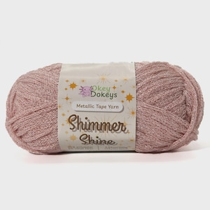 May include: A ball of pink metallic tape yarn with a label that reads "Okey Dokey's Shimmer Shine Metallic Tape Yarn". The yarn is 95% polyester and weighs 3.52oz/100g.